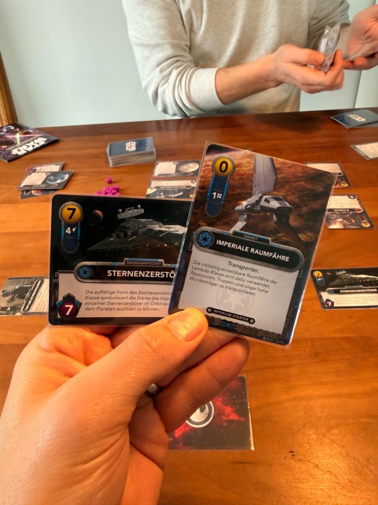 Eine Hand hält eine Spielkarte mit einer Fabrik und Rauch im Hintergrund.