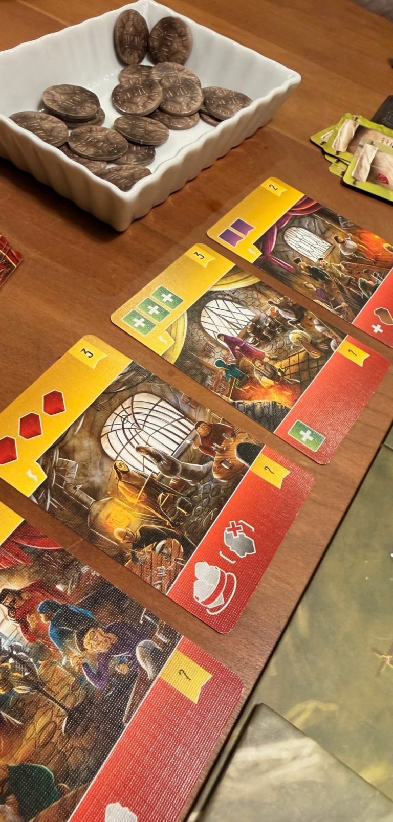 Spieltisch mit Karten und einer Schüssel mit Snacks. Karten zeigen Szenen aus einem Spiel.