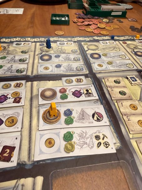 Brettspiel mit verschiedenen Karten, Münzen und Spielsteinen auf einem Tisch.
