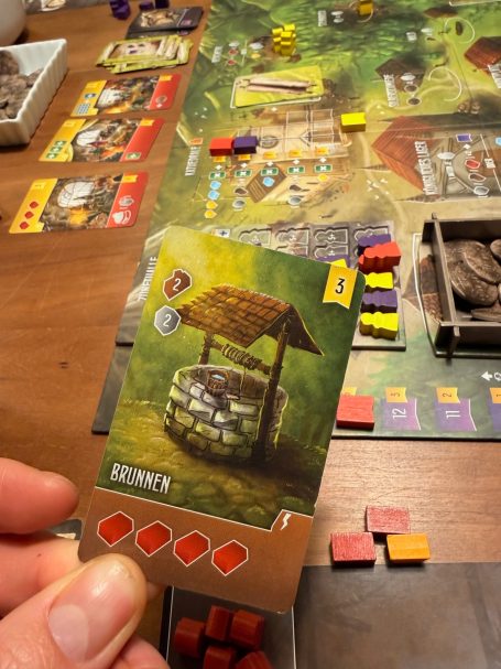 Karte mit Brunnen-Illustration und Spielsteinen auf einem Tisch.