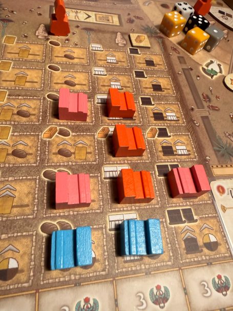 Brettspiel mit bunten Spielsteinen in Reihen angeordnet und verschiedenen Ressourcen.