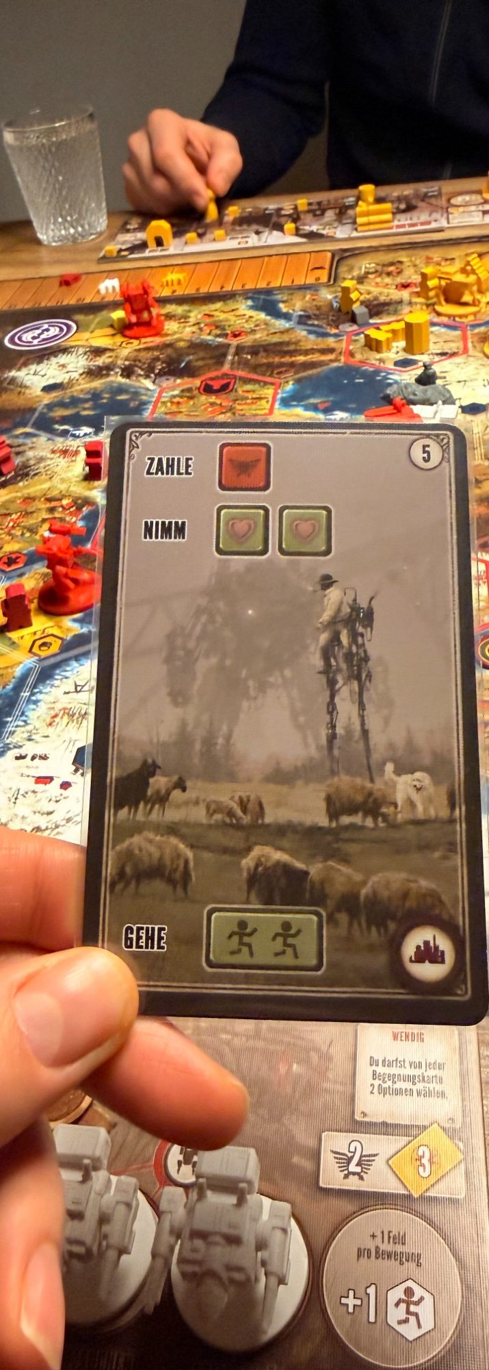 Eine Hand hält eine Spielkarte mit einer Fabrik und Rauch im Hintergrund.