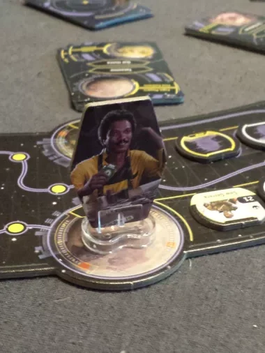 Eine Hand hält eine Spielkarte mit einer Fabrik und Rauch im Hintergrund.