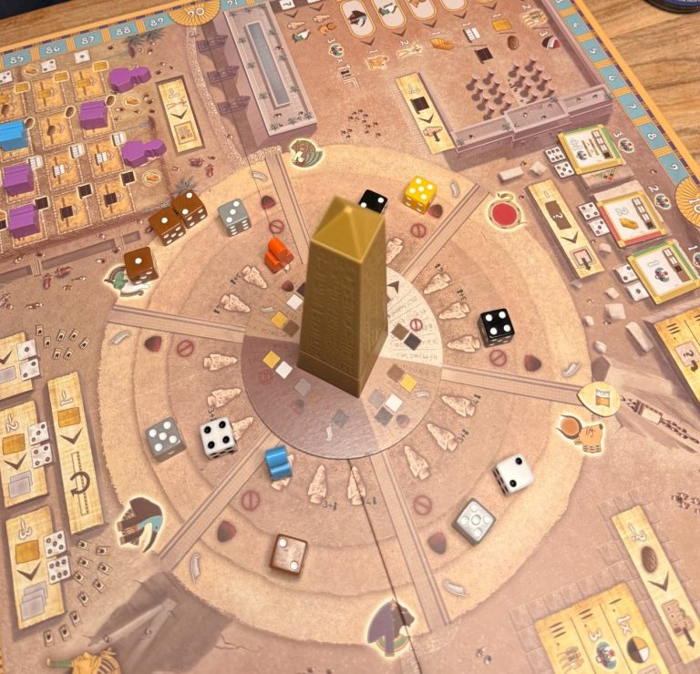 Brettspiel mit Spielbrett, Würfeln und verschiedenen Spielfiguren in einer runden Anordnung.