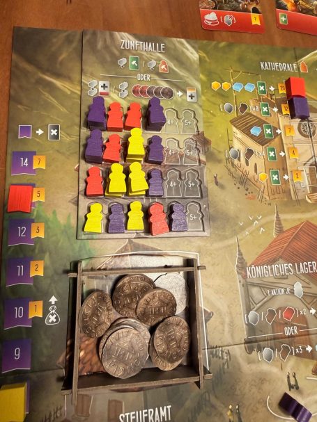 Spielbrett mit bunten Figuren und Münzen in einer Kiste.