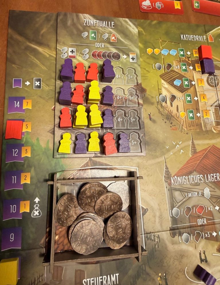 Spielfeld mit farbigen Spielfiguren, Spielkarten und einer Münzschale.