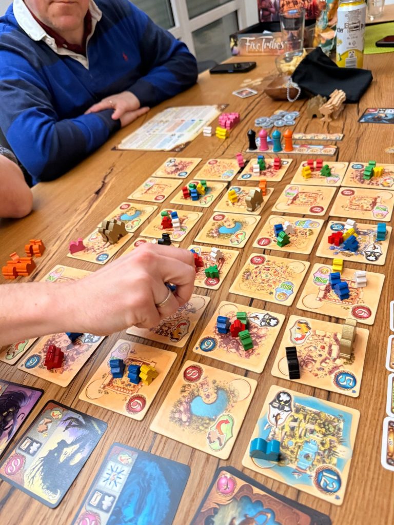 Ein Tisch mit einem Brettspiel, bunten Spielsteinen und Karten in verschiedenen Farben.