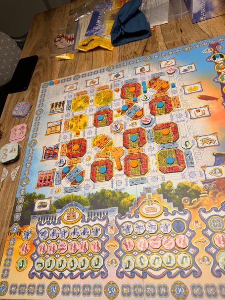 Brettspiel mit bunten Karten, Spielfiguren und Bewertungsfeldern auf einem Tisch.