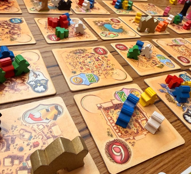Brettspiel mit bunten Holzfiguren und Spielkarten auf einem Tisch.