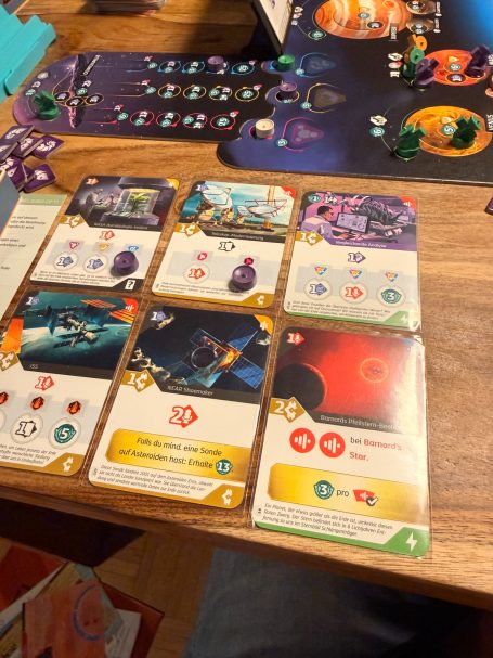 Spielbrett mit Karten, Würfeln und unterschiedlichen Spielfiguren in einer bunten Anordnung.