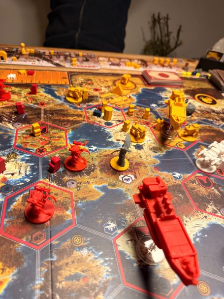 Spielbrett mit Schiffsfiguren in rot und gelb, umgeben von hexagonalen Feldern.