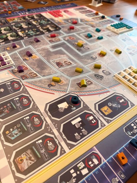 Brettspiel mit Spielbrett, farbigen Spielsteinen und Karten auf einem Tisch.