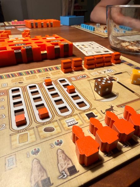 Brettspiel mit orangefarbenen Spielsteinen und Würfeln auf einem Holztisch.