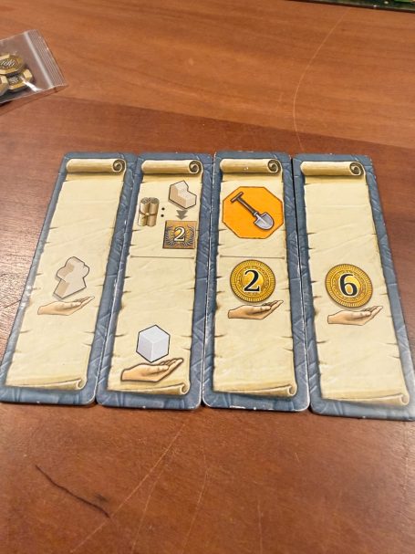 Vier Spielkarten mit verschiedenen Symbolen, Zahlen und Goldmünzen.