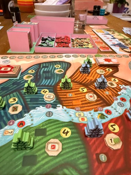 Brettspielszene mit verschiedenen Ressourcen und Spielerfiguren auf einem farbenfrohen Spielbrett.