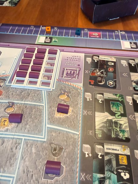 Brettspiel mit Spielsteinen und Karten auf einer grauen, runden Spielfläche.
