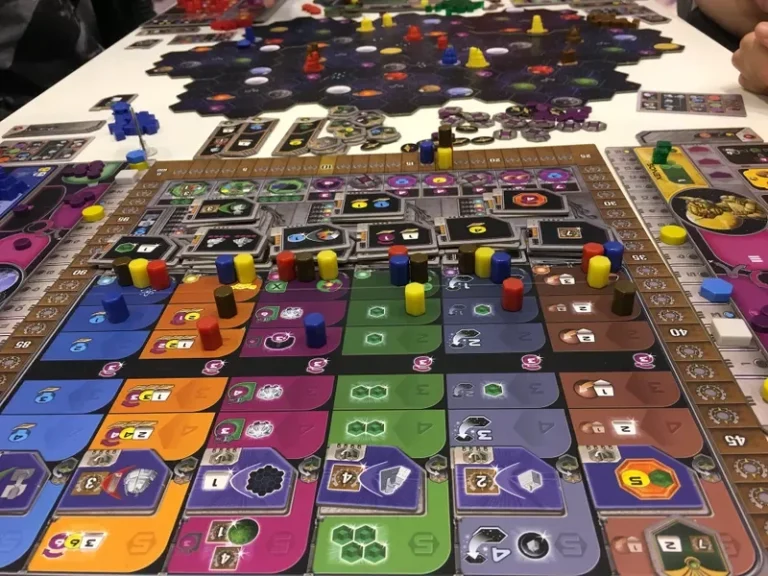 Spielbrett mit bunten Spielfiguren und einem zentralen gelben Punkt in orangefarbener Umgebung.