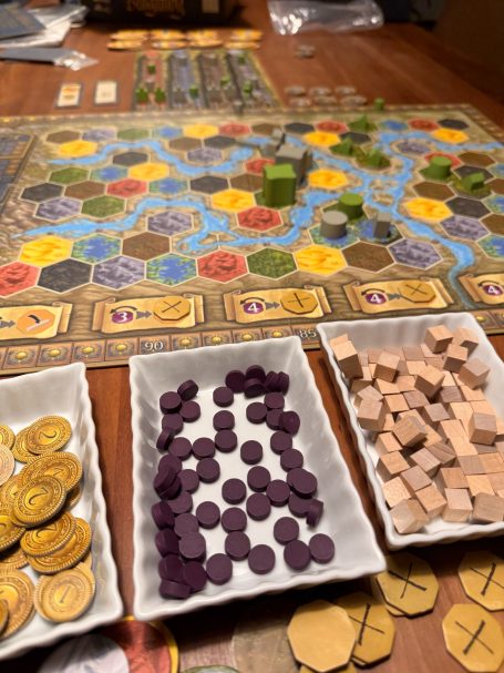 Brettspielszene mit Ressourcen, Spielsteinen und Spielbrett in bunten Farben.