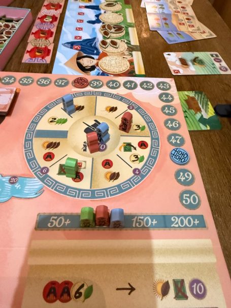 Brettspiel mit bunten Spielsteinen, Punkten und Aktionsfeldern auf einem Tisch.