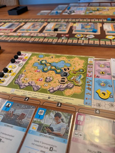 Brettspiel mit Spielbrett, Karten und Spielfiguren auf einem Holztisch.