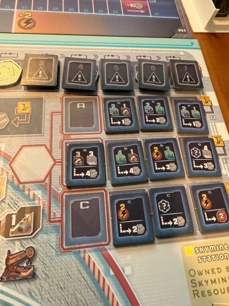 Brettspiel mit verschiedenen Spielsteinen und Symbolen, angeordnet in einem Raster.