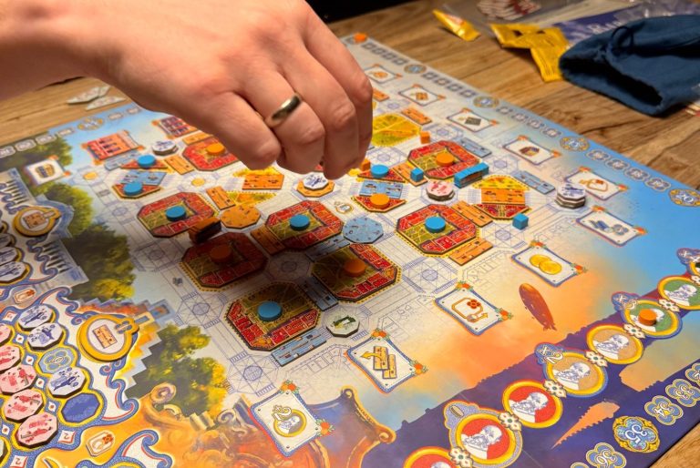 Hand platziert Spielsteine auf einem bunten Spielbrett mit verschiedenen Symbolen und Feldern.