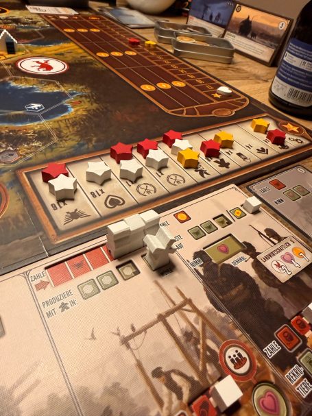 Brettspiel mit verschiedenen farbigen Spielfiguren und Karten auf einem Holztisch.