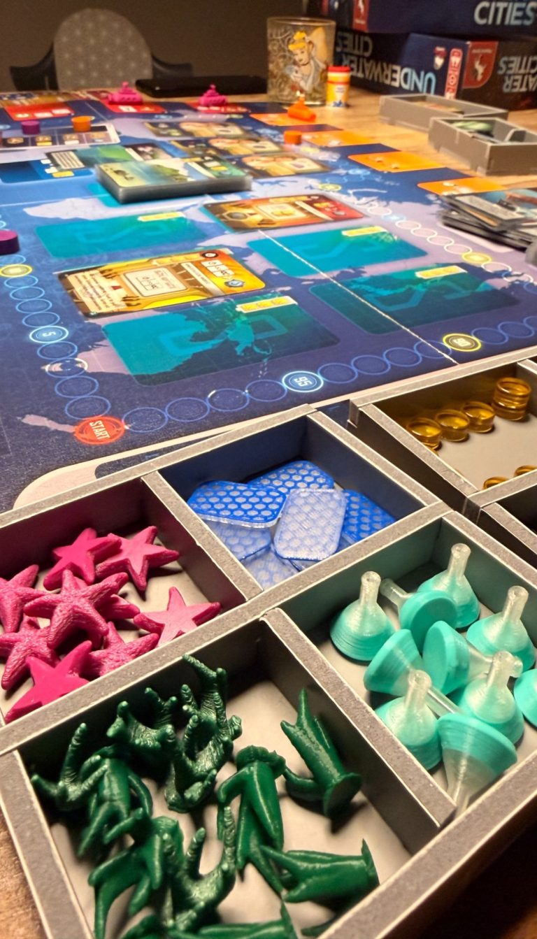 Spieler hält zwei Aktionskarten mit Obst, Nüssen und einem Segelboot, umgeben von Spielbrett.