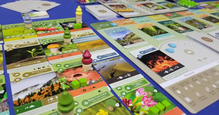Spielbrett mit bunten Spielfiguren und einem zentralen gelben Punkt in orangefarbener Umgebung.
