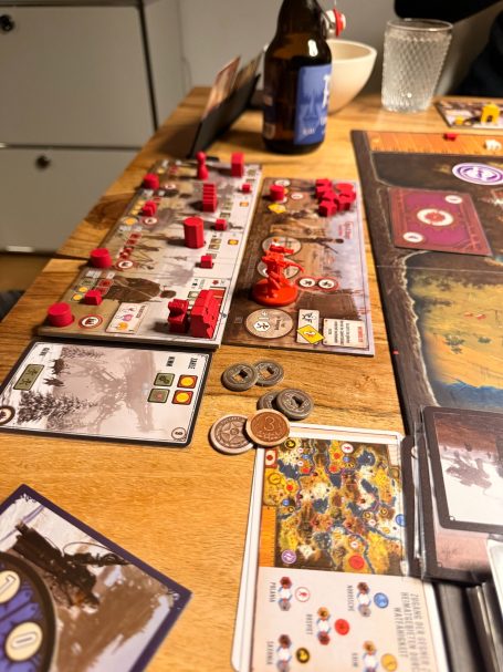 Spielbrett mit Würfeln, Spielsteinen und Geldmünzen auf einem Tisch.