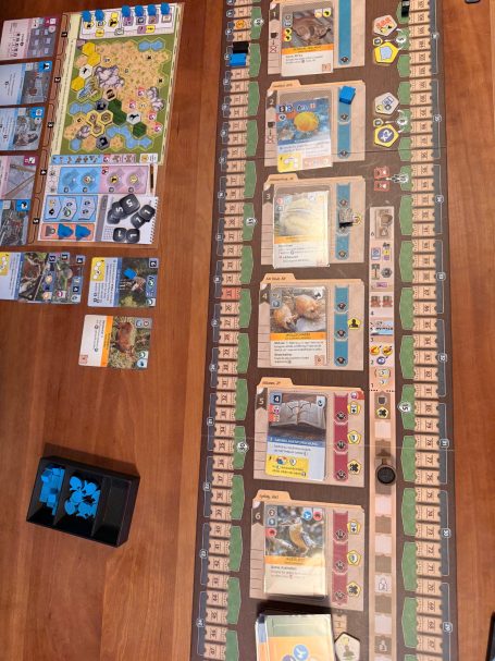 Brettspiel mit Ressourcen und Karten auf einem Tisch, verschiedene Spielfelder und Marker.