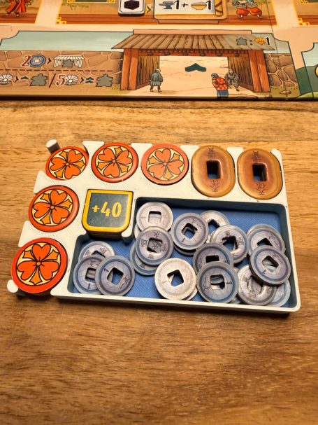 Spielmaterial mit Spielsteinen und Geldmarken auf einem Holztisch.