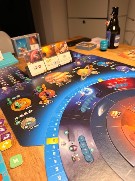 Brettspiel mit bunten Spielfiguren, Karten und Spielmarken auf einem Tisch.