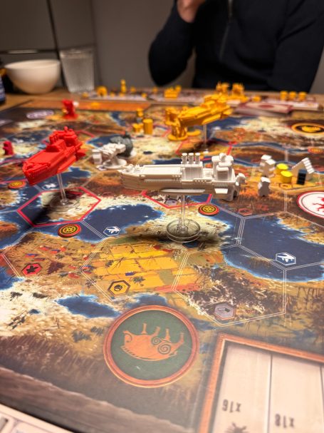 Detailaufnahme eines Brettspiels mit Figuren, Holzspielsteinen und einer Landschaftskarte.