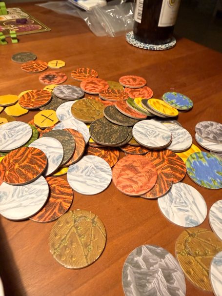 Bunte Spielchips aus verschiedenen Materialien auf einem Holztisch verteilt.