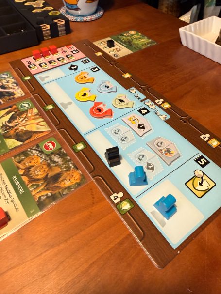 Brettspiel mit verschiedenen Spielfiguren und Karten auf einem Holztisch.
