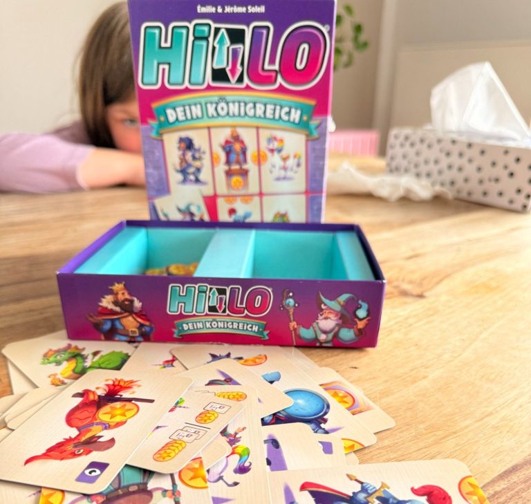 Spiel "HIT LO" mit offenen Karten und einer Box, im Hintergrund ein Kind.